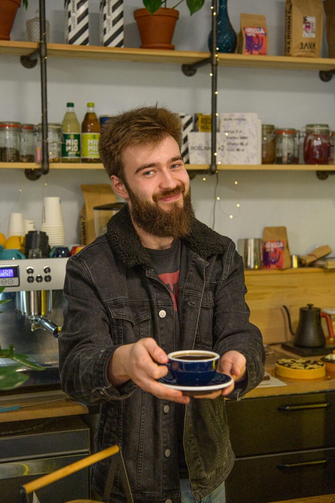 uśmiechnięty mężczyzna z brodą podaje kawę klientowi kawiarni, reklama cukierni, kawiarni, zdjęcie wizerunkowe Szczecin